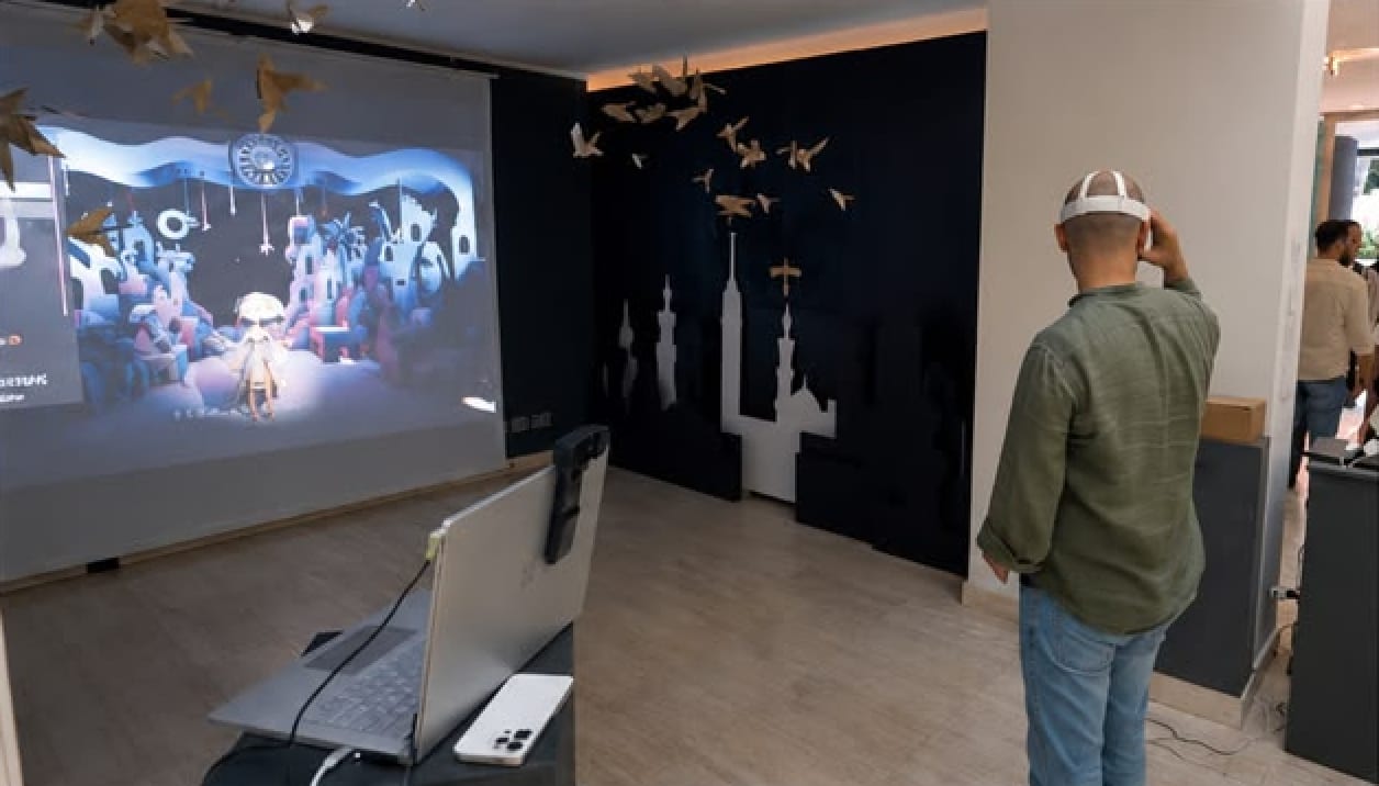 A visitor wearing the VR headset, seen from behind, facing the CLAP FOR ME projection