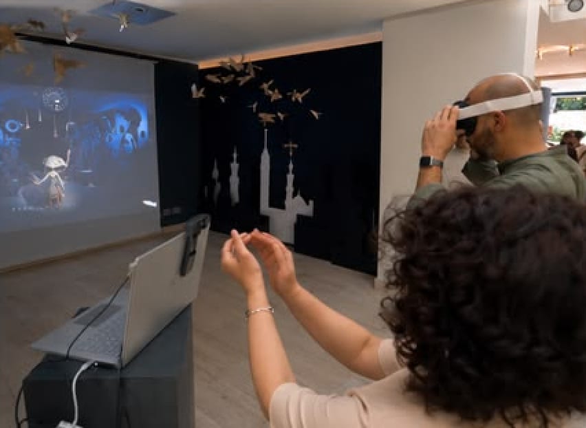 A woman claps as a man beside her wears the CLAP FOR ME headset, facing the projection